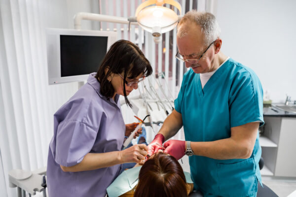 Team of professional dentists, man and woman, doing the treatment for young woman patient in their surgery dental clinic.